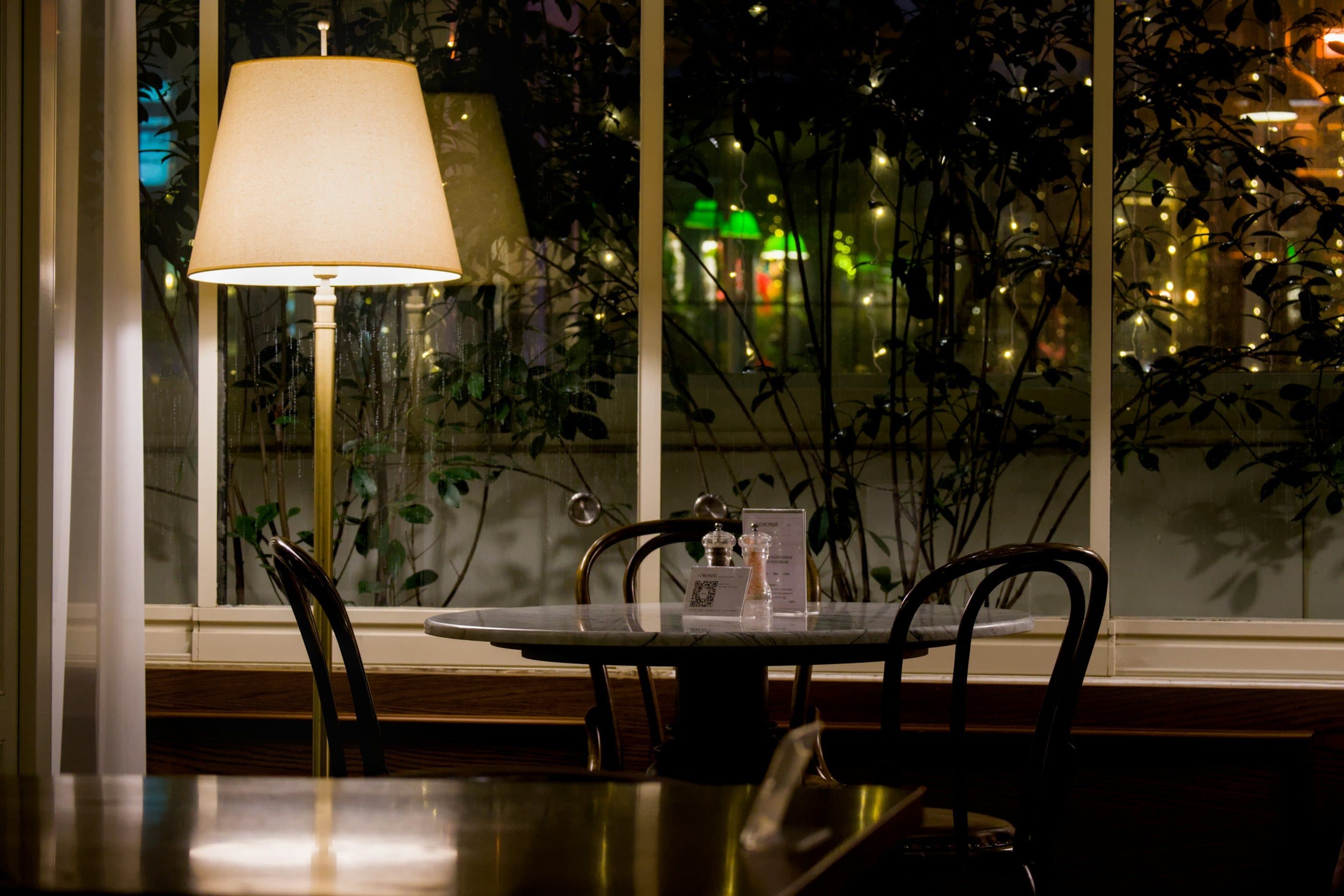 A quiet café table and bentwood chairs beside a lamp-lit window at night