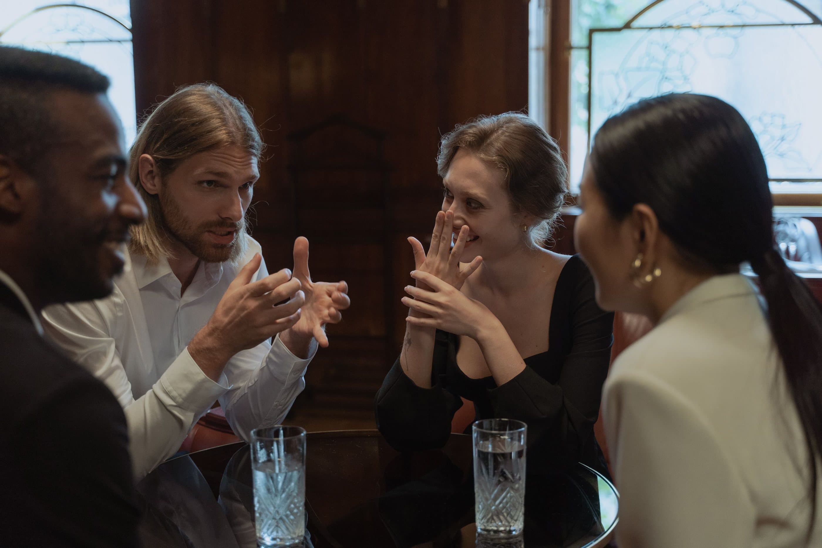 Four professionals share an animated conversation around a table in a dim, wood-panelled room