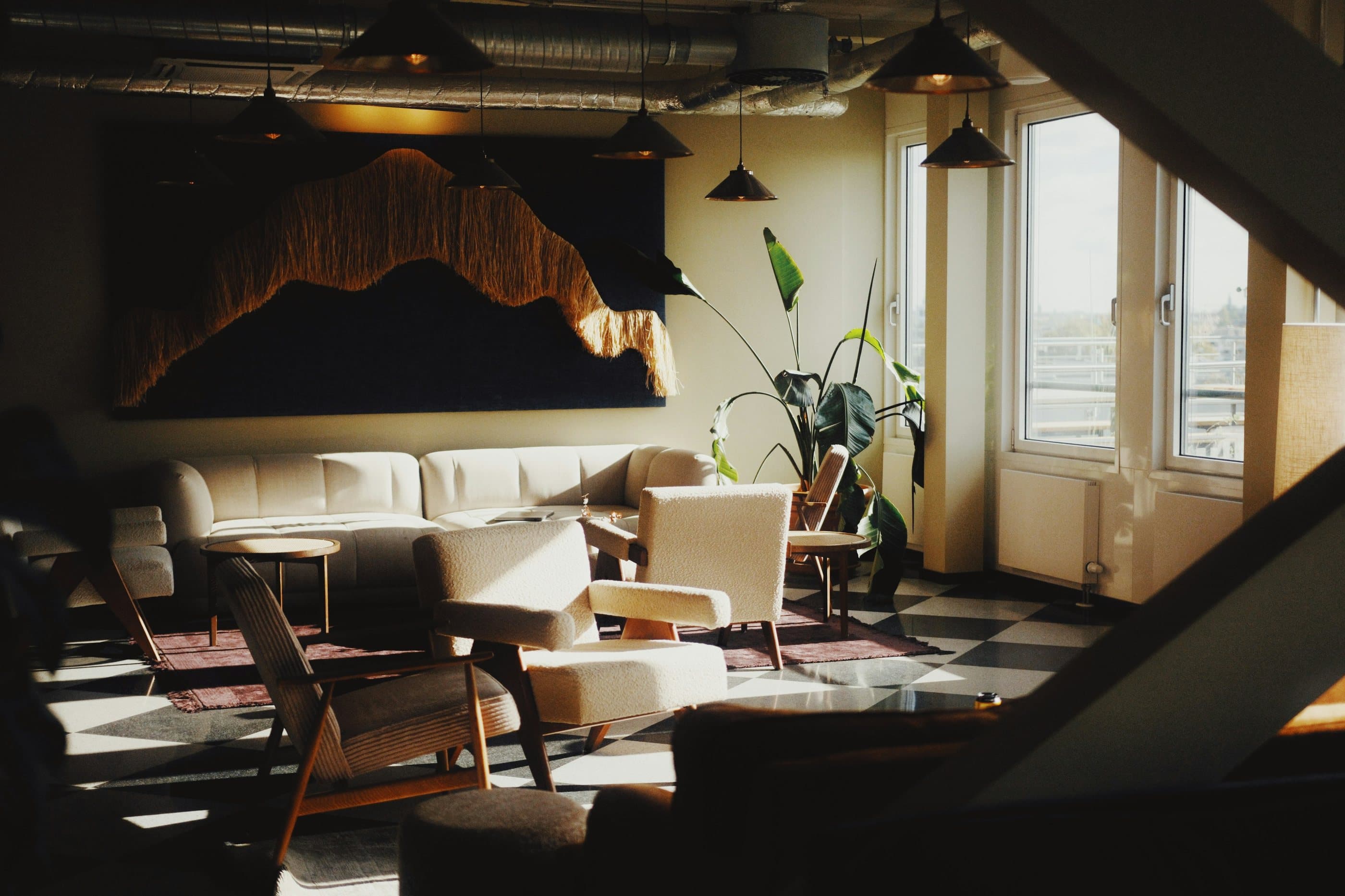 Afternoon light falls across a calm lounge of cream sofas, mid-century armchairs and a checkerboard floor beneath a large textured artwork